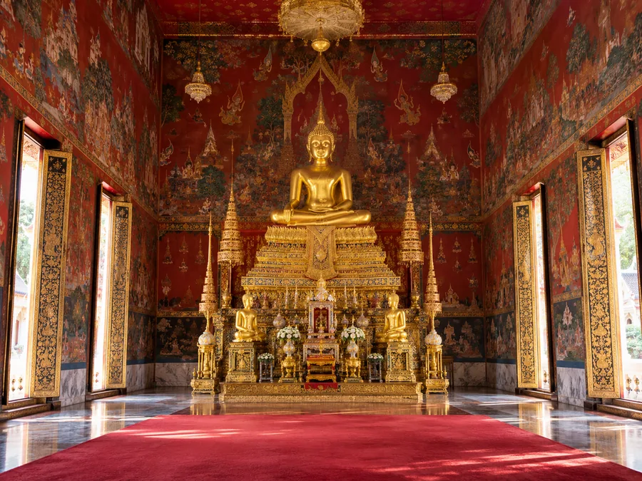 พระพุทธรูปปางนั่งสีทองบนฐานชุกชีปิดทองในพระอุโบสถที่มีจิตรกรรมฝาผนัง