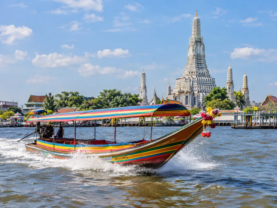 เรือหางยาวไม้แล่นฉิวไปตามแม่น้ำเจ้าพระยา โดยมีพระปรางค์สีขาวของวัดอรุณอยู่ด้านหลัง